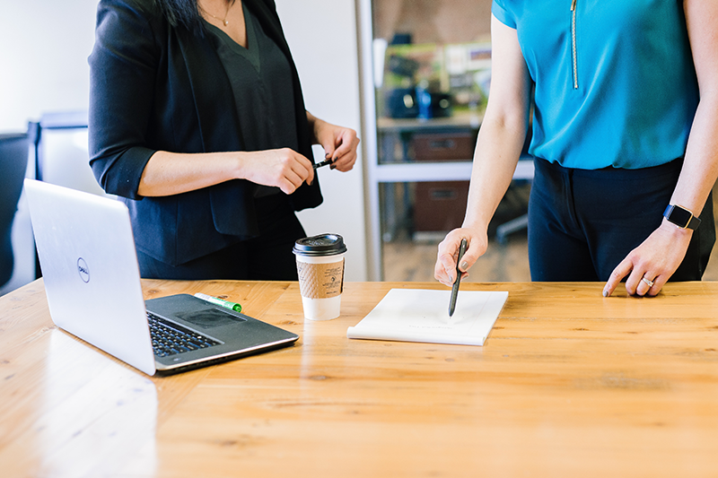 women in business stood at a desk with a takeout coffee